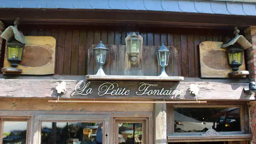 Centraal uithangbord in schrijfletter van La Petite Fontaine in Achouffe onder een rij van vijf traditionele, rustieke lantaarns