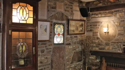 Intérieur rustique en briques et pierres du restaurant La Petite Fontaine à Achouffe avec mobilier en bois et vitraux illuminés