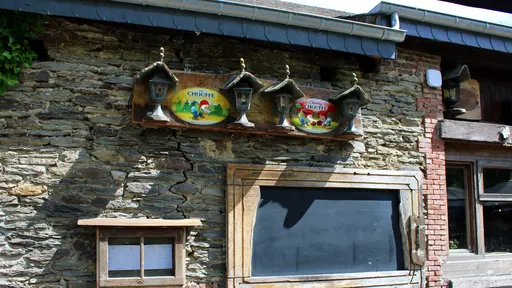 Ardense stenen muur van restaurant La Petite Fontaine in Achouffe met een groot krijtbord voor de wekelijkse suggesties, een vitrine voor het menu en Chouffe reclameverlichting