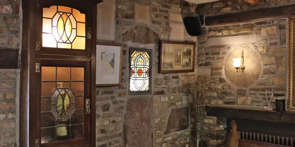 Intérieur rustique en briques et pierres du restaurant La Petite Fontaine à Achouffe avec mobilier en bois et vitraux illuminés